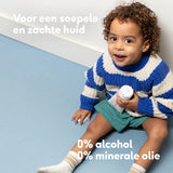 Sfeerbeeld van een guitig lachend jongetje met krullen korte broek en gebreide trui met de tekst 'Voor een soepele en zachet huid. 0% alcohol. 0% minerale olie'