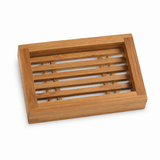 Bamboe zeepbakje met open lattenstructuur op een witte studioachtergrond, gefotografeerd onder een lichte hoek met zachte fotorealistische schaduw. Het natuurlijke hout en minimalistische ontwerp geven het accessoire een warme en moderne uitstraling.