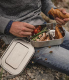 Ingezoomd sfeerbeeld van een sportieve man die de lunchbox gevuld met groenten en brood in een outdoor setting op zijn schoot heeft rusten