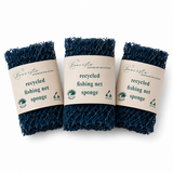 Minimalistisch productshot van donkerblauwe gerecyclede fishing net sponzen met beige Boavista-label op een witte studioachtergrond. Het label toont het Boavista-logo, duurzame iconen en de tekst ‘recycled fishing net sponge’. Zachte professionele belichting en een subtiele fotorealistische schaduw geven het product een premium en duurzame uitstraling.