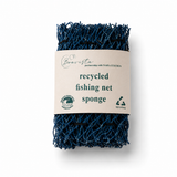 Minimalistisch productshot van donkerblauwe gerecyclede fishing net spons met beige Boavista-label op een witte studioachtergrond. Het label toont het Boavista-logo, duurzame iconen en de tekst ‘recycled fishing net sponge’. Zachte professionele belichting en een subtiele fotorealistische schaduw geven het product een premium en duurzame uitstraling.