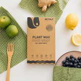 Flatlay sfeerfoto van Plant Wax Food Wrap verpakking op een witte tafel waarop groene geruite Retulp plant wax food wraps liggen die in gebruik zijn. Omringd door limoenen, citroen, gember, blauwe bessen en een houten vork. Met zachte natuurlijke belichting voor een frisse, duurzame en premium uitstraling